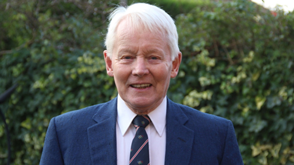 Peter Warden is pictured smiling. He is standing in front of a hedge. He is wearing a suit and tie.